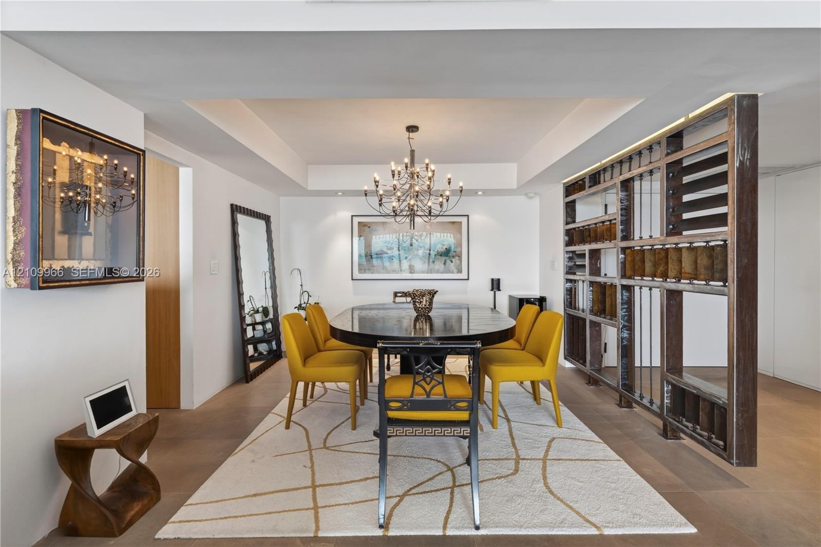 Tray ceiling with recessed lighting, custom floor-to-ceiling metal and glass open-frame partition, multi-arm chandelier, and wide-plank wood-finish fl