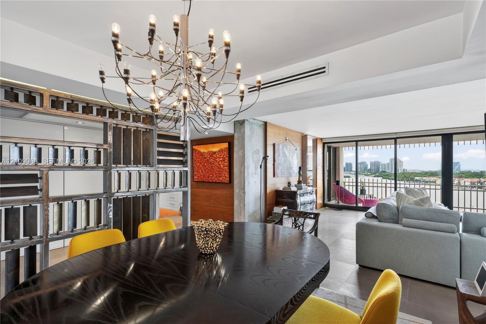 Open-concept interior featuring a multi-arm modern chandelier, custom decorative metal partition wall, wood-paneled feature wall, floor-to-ceiling gla