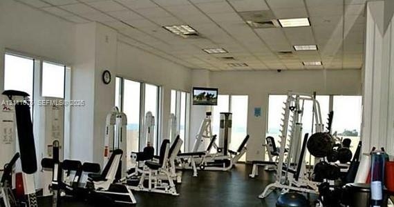 Fitness center featuring floor-to-ceiling windows, drop ceiling with recessed lighting, and rubberized flooring