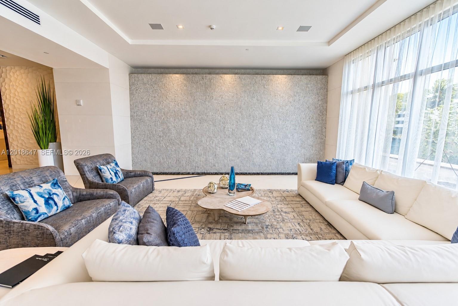 Floor-to-ceiling windows with layered drapery, recessed tray ceiling lighting, textured stone-finish accent wall, and polished stone-finish flooring
