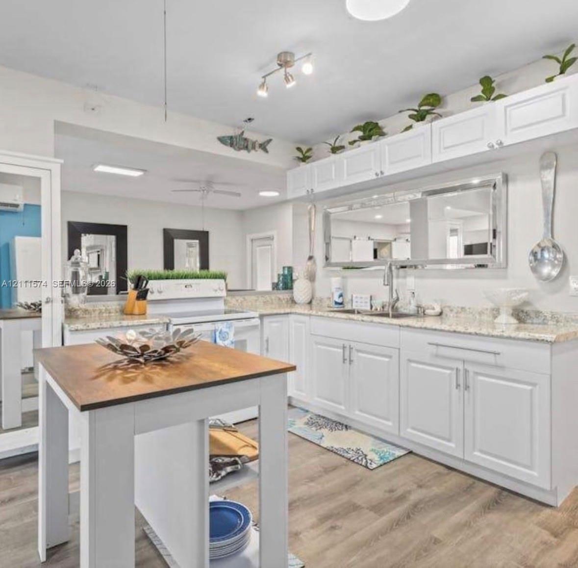 Kitchen featuring white shaker-style cabinetry, stone-finish countertops, wood-finish flooring, a stainless steel undermount sink, and a center island