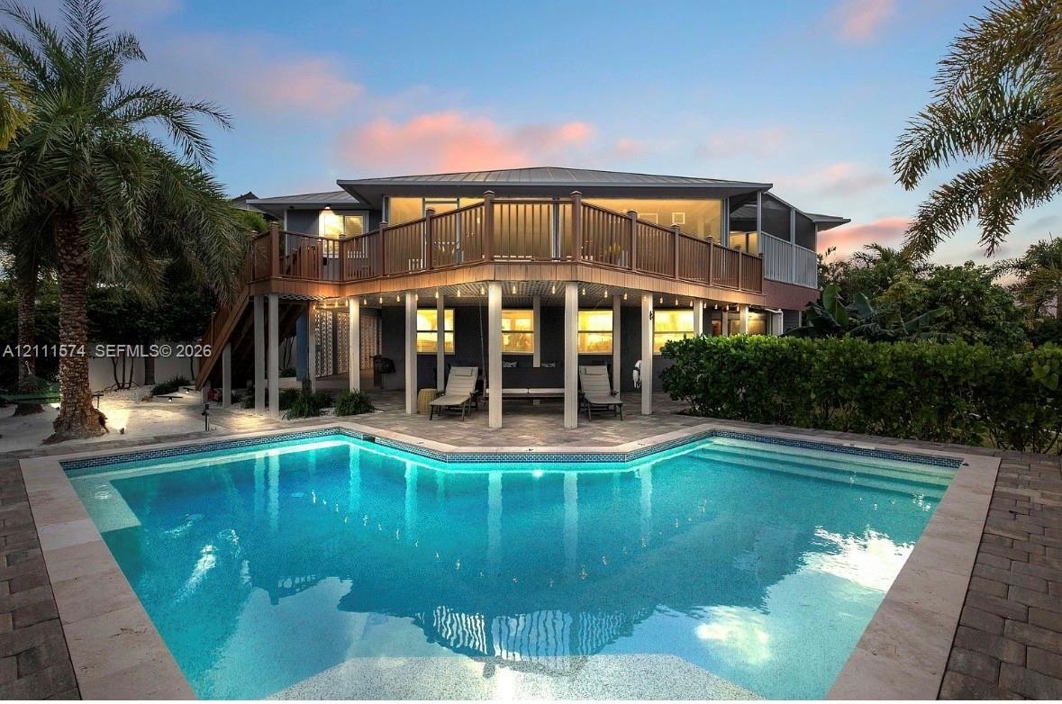 Multi-level elevated home featuring a wrap-around wooden deck, a ground-level covered patio area with support columns, and an inground swimming pool w