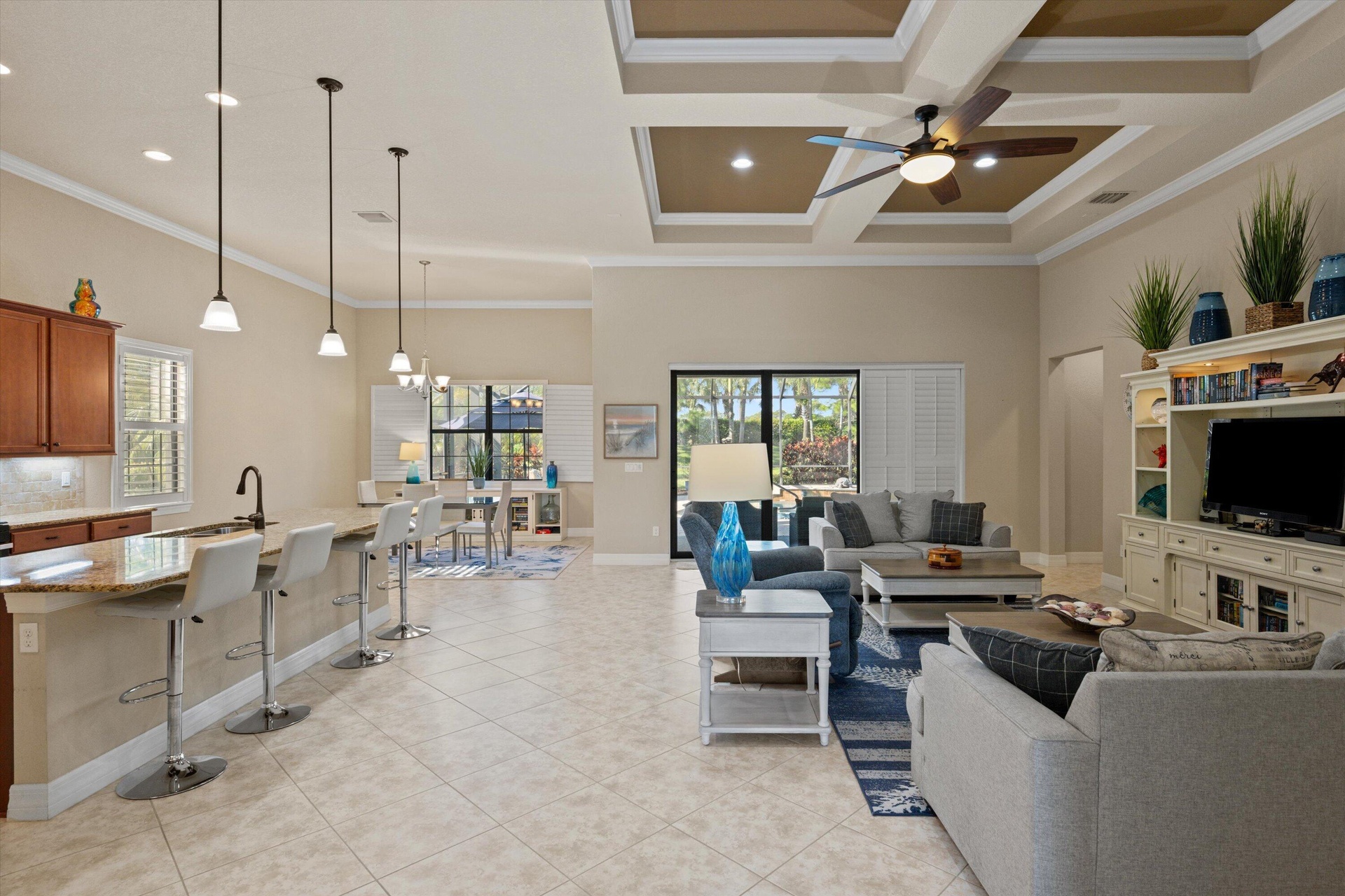 Open-concept layout featuring a coffered ceiling, recessed lighting, tile flooring, built-in entertainment cabinetry, and a kitchen island with pendan