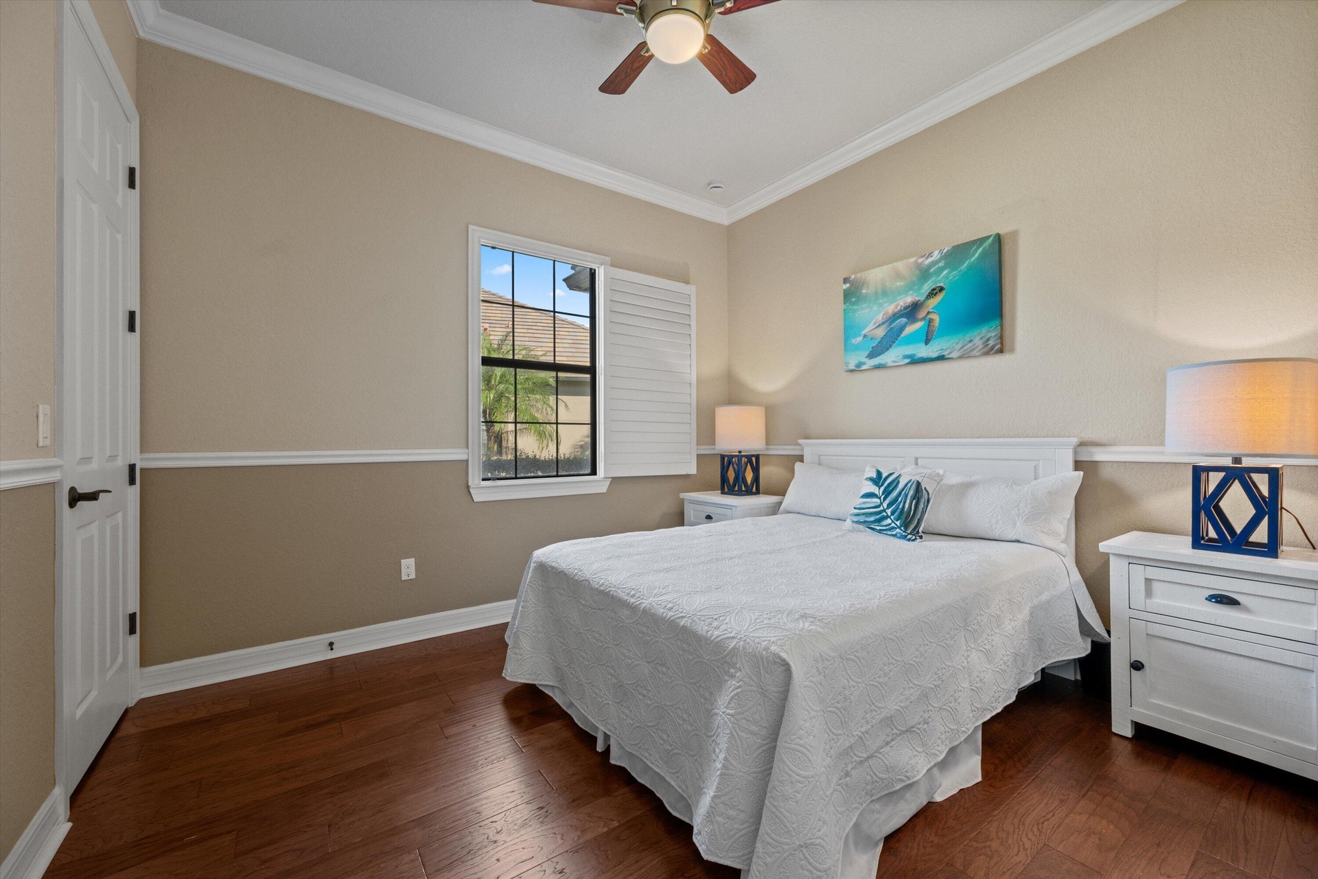 Wood-finish flooring, multi-pane window with plantation shutters, ceiling fan, and chair rail molding