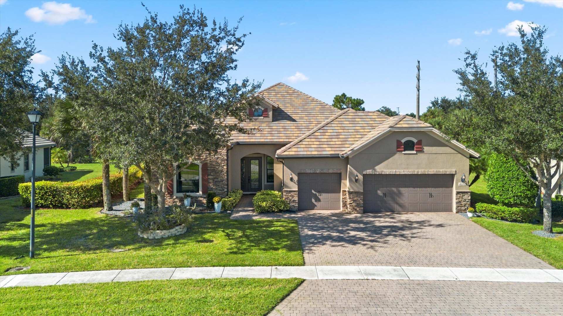 Stucco exterior residence featuring stone veneer accents, a multi-car garage, a paver driveway, and a tiled roof