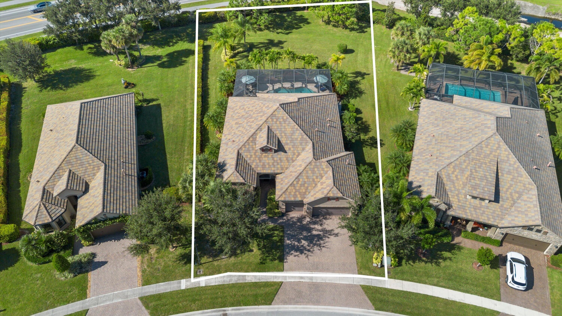 Aerial perspective featuring a paved driveway, a multi-gabled roof, an enclosed screened-in pool, and extensive lawn landscaping