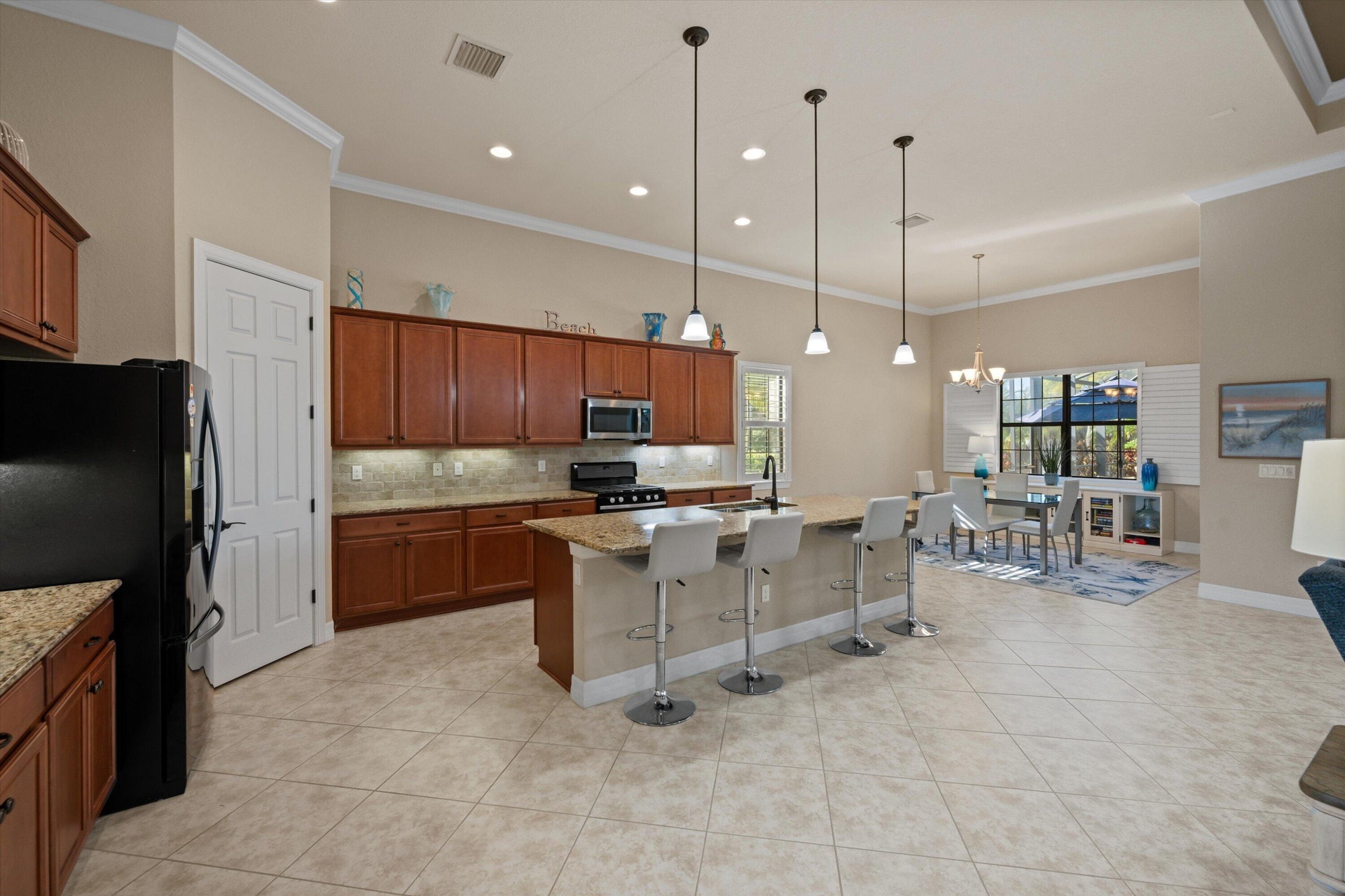 Kitchen featuring cabinetry with stained wood finish, stone-surfaced countertops, a center island with bar seating, pendant lighting, and tile floorin