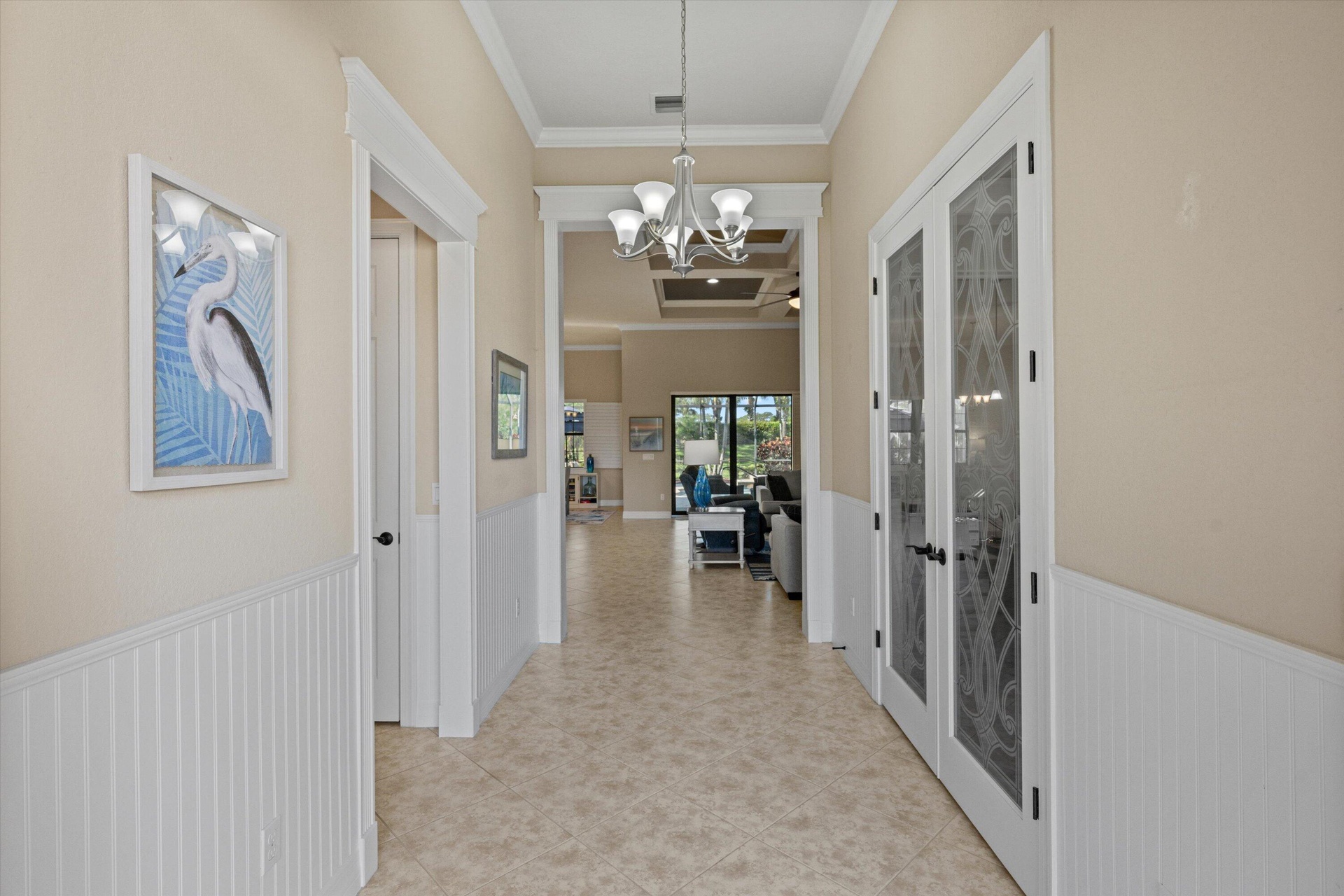 Foyer featuring white beadboard wainscoting, crown molding, tile flooring, a multi-arm chandelier, and glass-paneled French doors with decorative etch