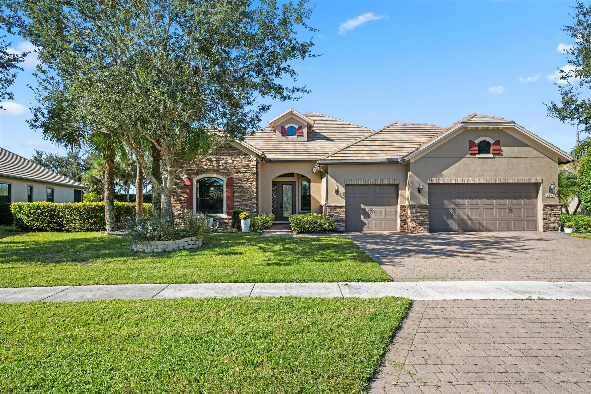Single-story residence featuring a stone and stucco facade, concrete tile roof, paved driveway, and arched entryway