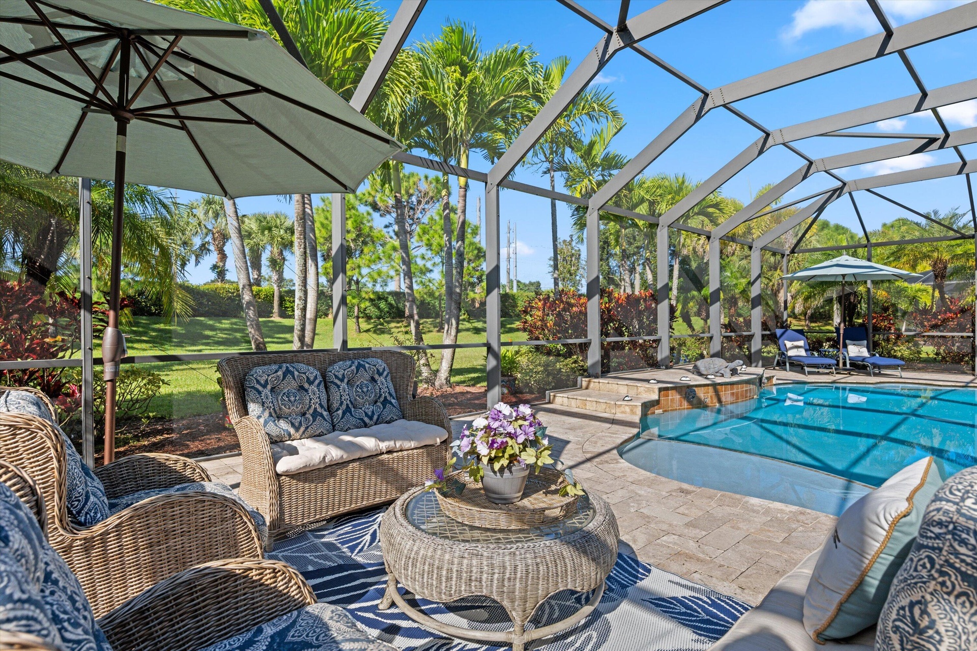 Screened-in lanai featuring a paver deck, built-in swimming pool with elevated spa, and surrounding mature palm trees