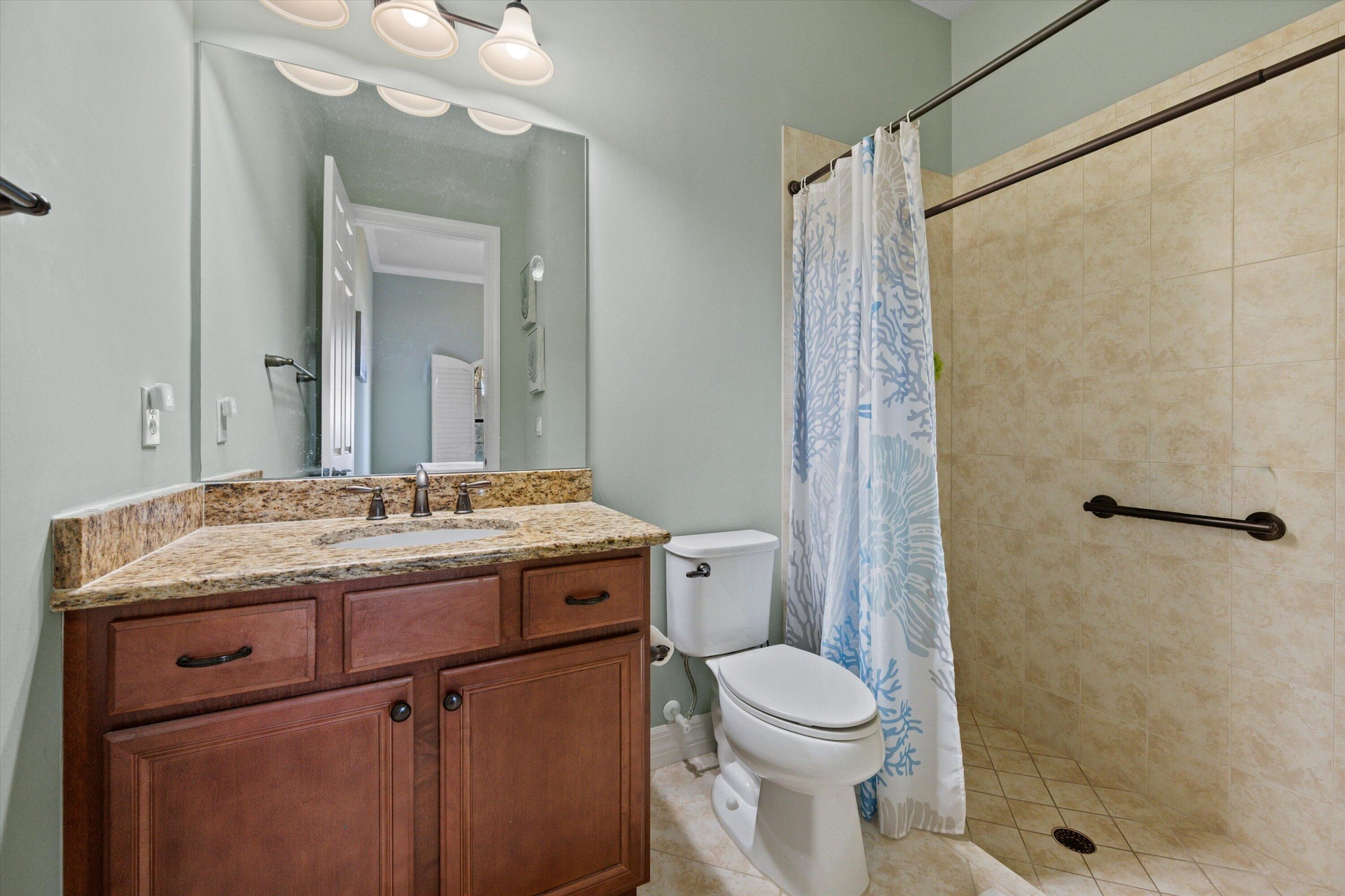 Bathroom featuring wood-finish cabinetry, stone-texture countertop, integrated sink, and walk-in shower with tile surround