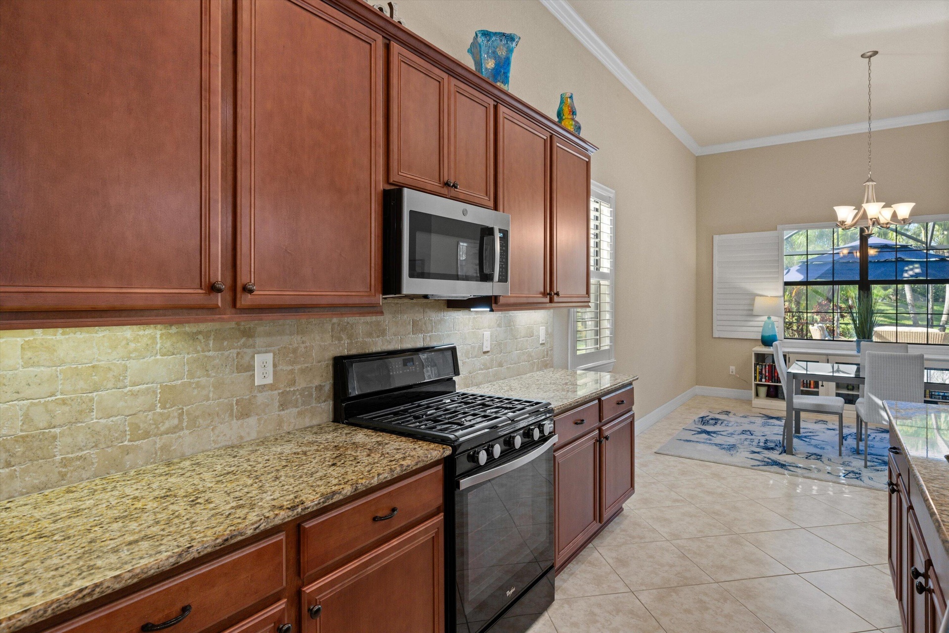 Kitchen featuring raised-panel wood cabinetry, natural stone tile backsplash, stone countertops, stainless steel microwave, and tile flooring