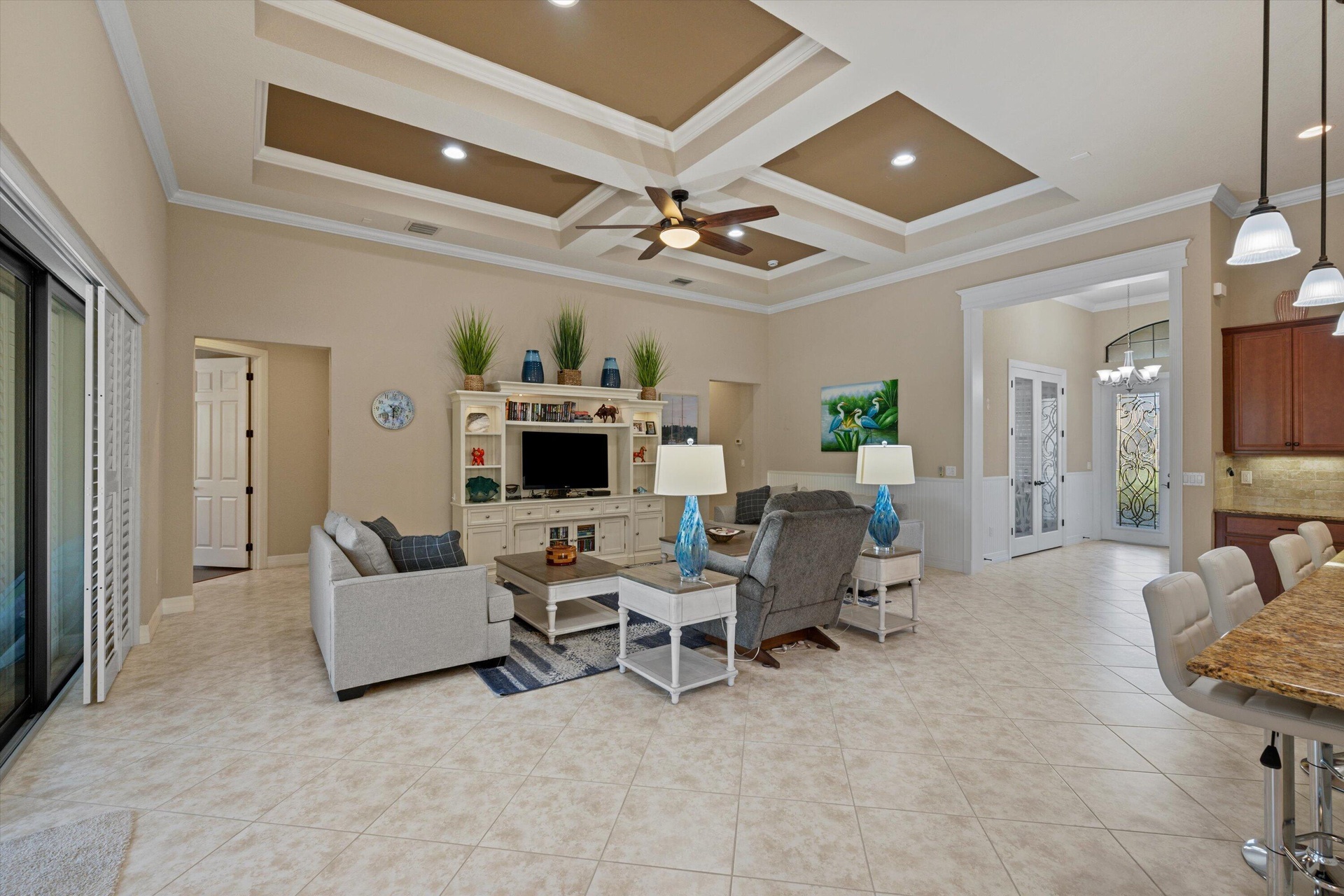 Tray ceiling with recessed lighting and a central ceiling fan, built-in media cabinetry, tile flooring, stone-surfaced kitchen island, and pendant lig