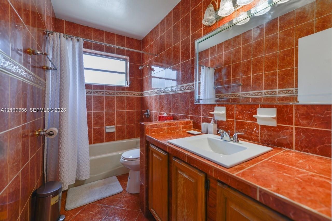 Bathroom featuring full-height decorative tile wall finishes, an integrated vanity countertop with a drop-in sink, wood-finish cabinetry, a large wall