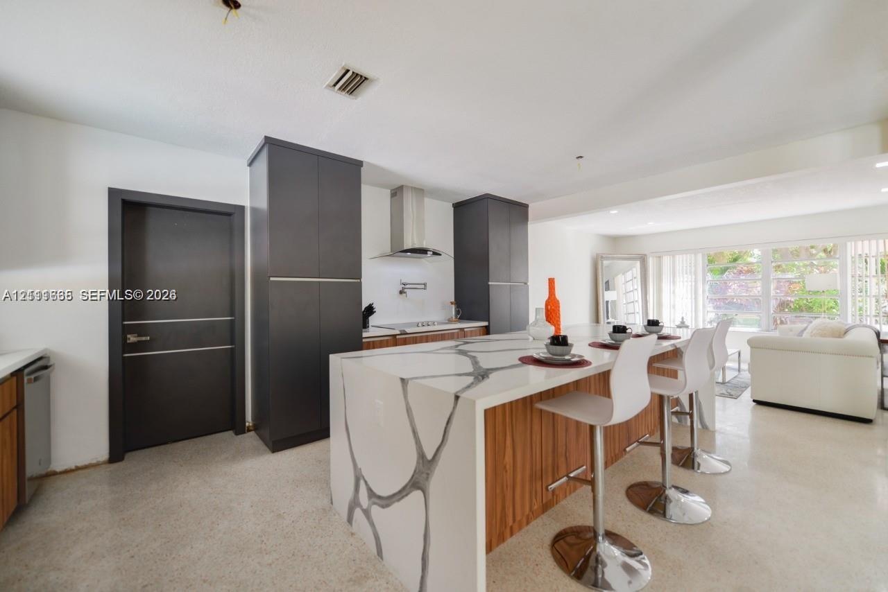 Kitchen featuring a waterfall-edge island with stone-finish countertops and wood-finish cabinetry, floor-to-ceiling dark charcoal pantry units, and a 