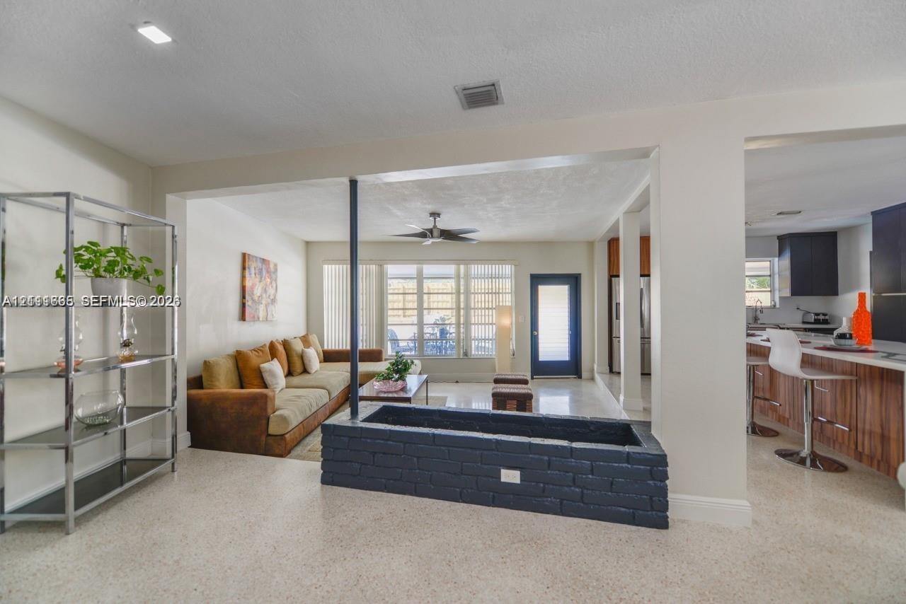 Open-concept interior featuring light-toned stone-finish flooring, recessed lighting, and a painted brick built-in planter with a central support pill