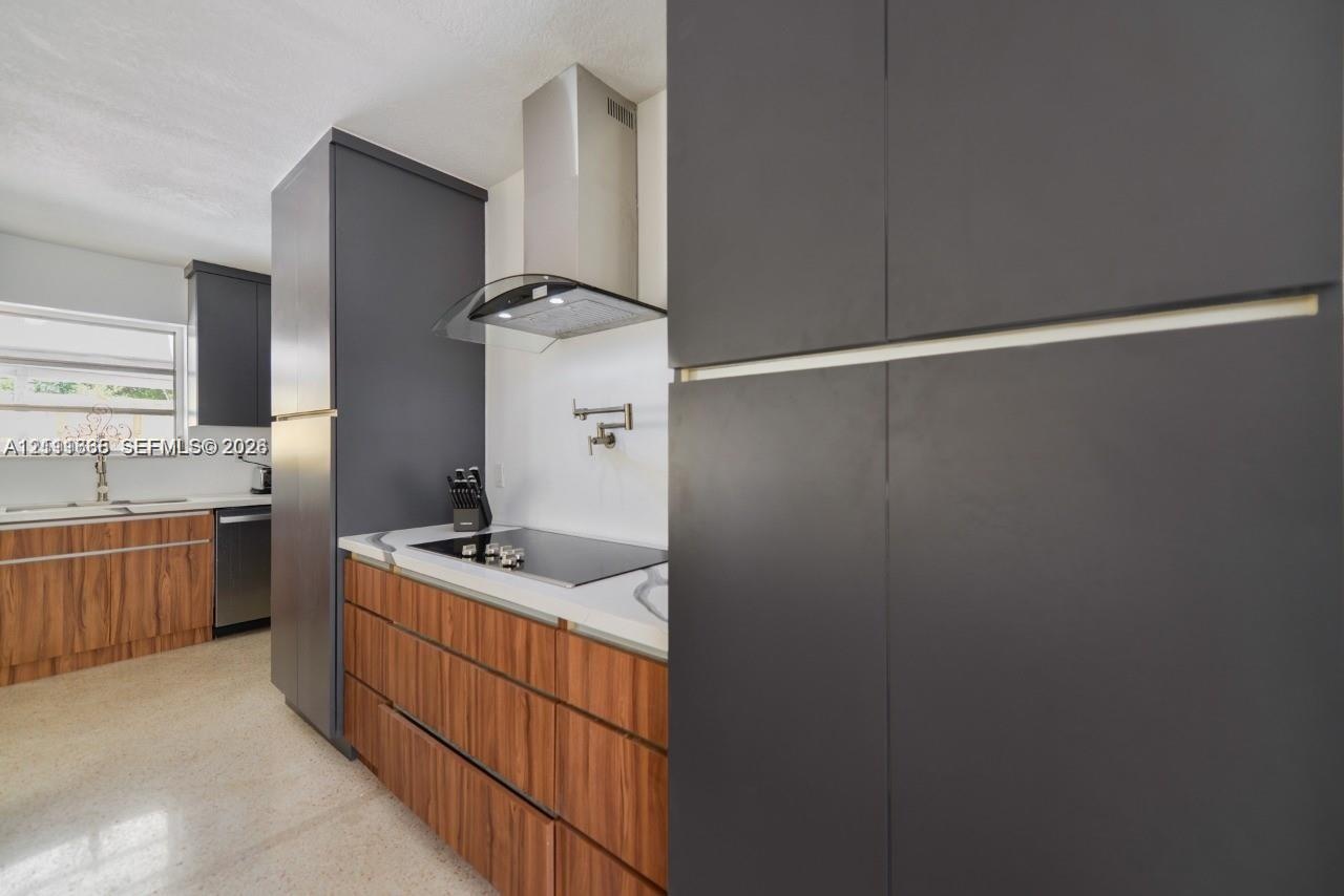 Kitchen featuring custom flat-panel cabinetry with wood-finish lower cabinets and matte charcoal upper cabinetry, stainless steel range hood, integrat