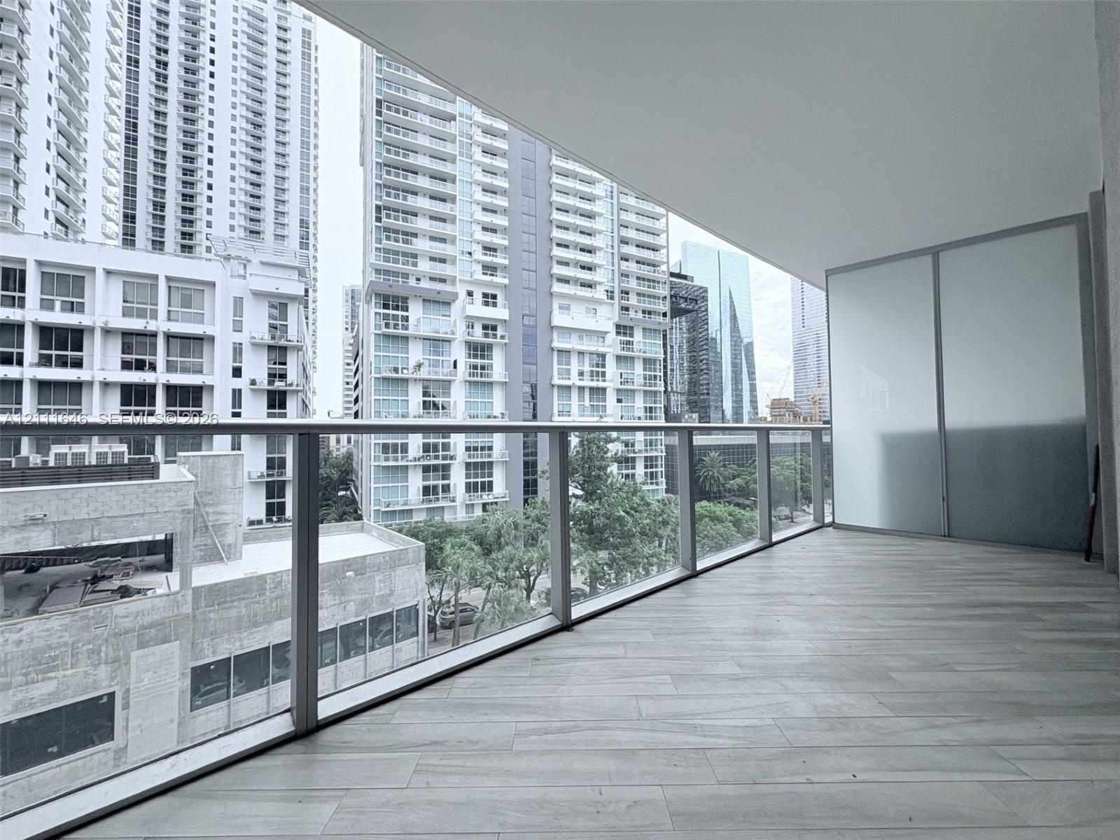 Covered balcony featuring wood-finish tile flooring, glass panel railings, and frosted privacy screening