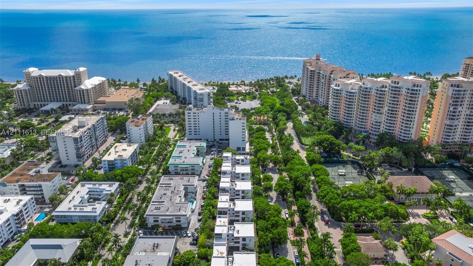 Aerial perspective of a coastal residential community featuring multiple high-rise structures, landscaped green space, tennis courts, and immediate pr