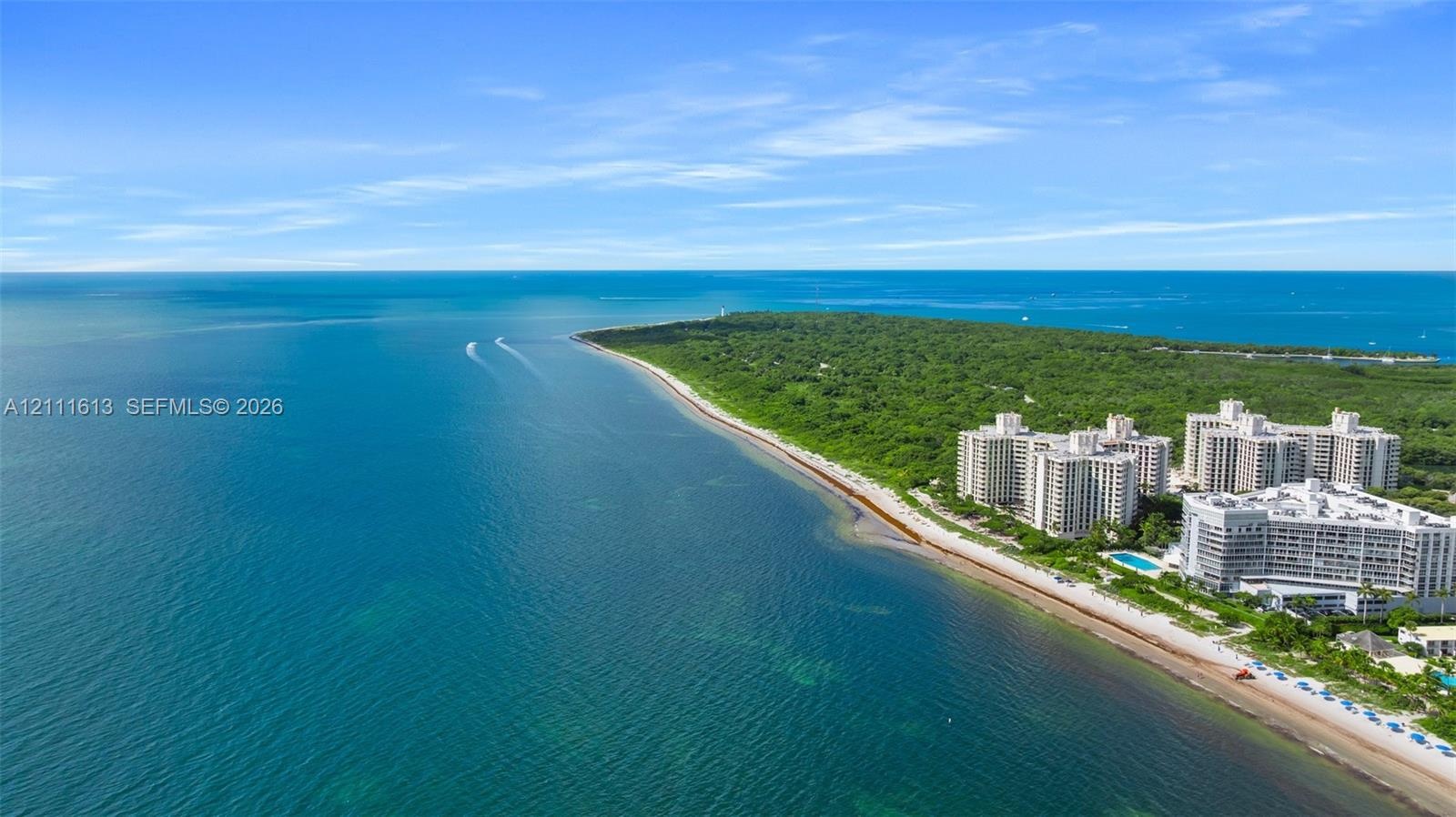 Aerial perspective of coastal multi-story residential buildings featuring immediate proximity to the shoreline and direct access to expansive sandy be
