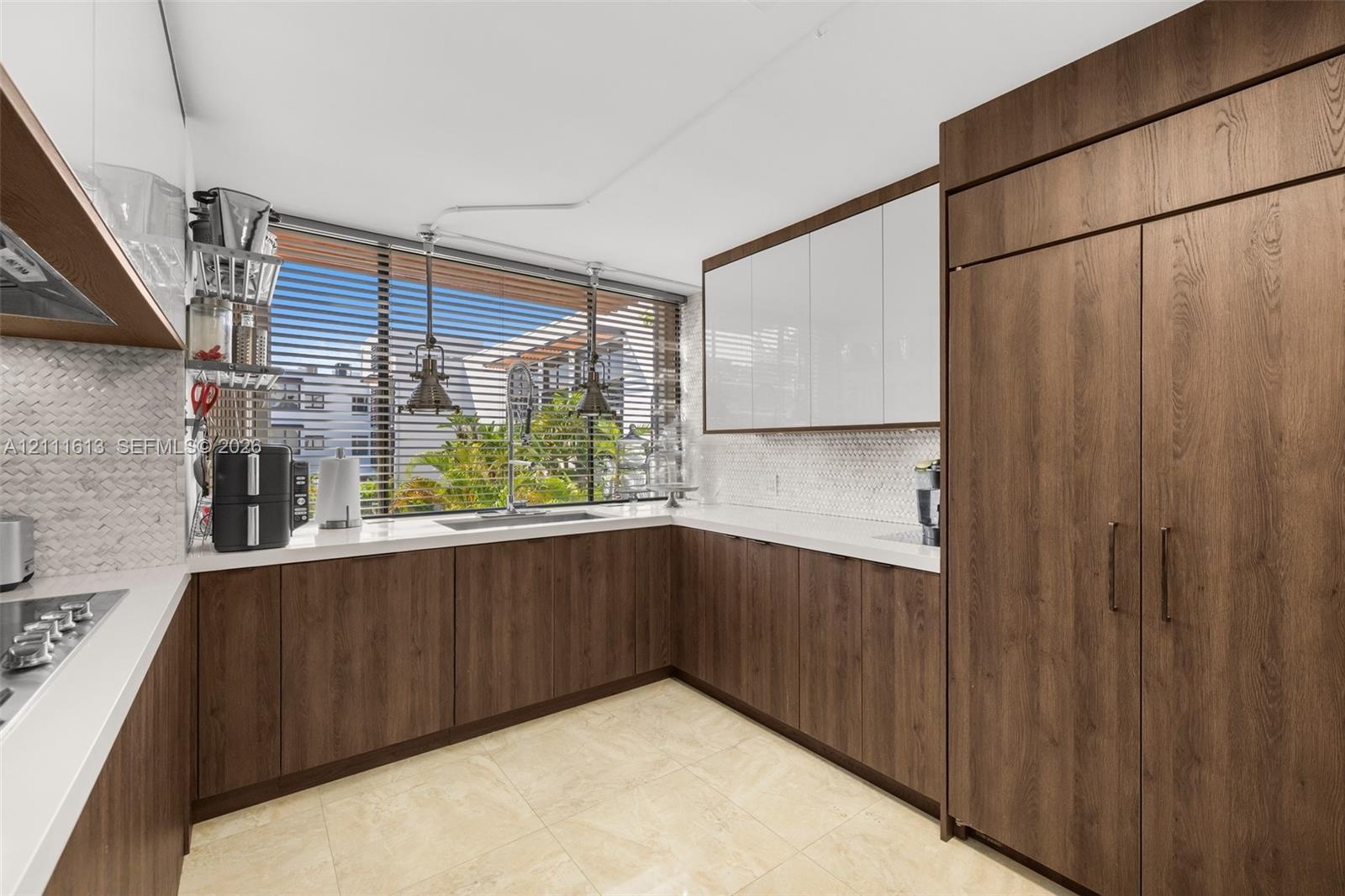 Kitchen featuring two-tone cabinetry with wood-finish lower units and high-gloss white upper cabinets, light-toned stone countertops, hexagonal mosaic