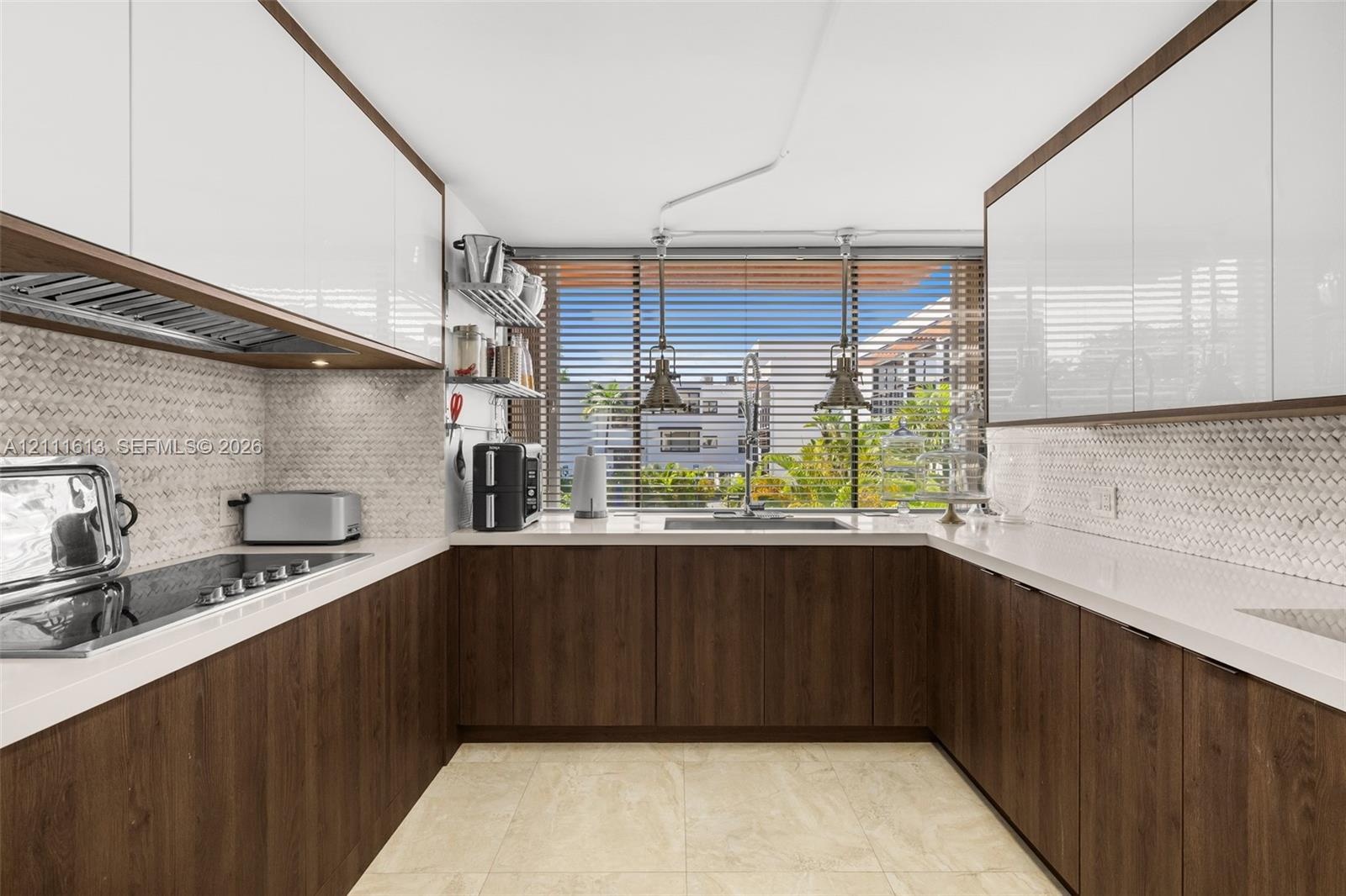 Kitchen featuring two-tone cabinetry with wood-finish lower units and high-gloss upper cabinets, solid-surface countertops, mosaic tile backsplash, an