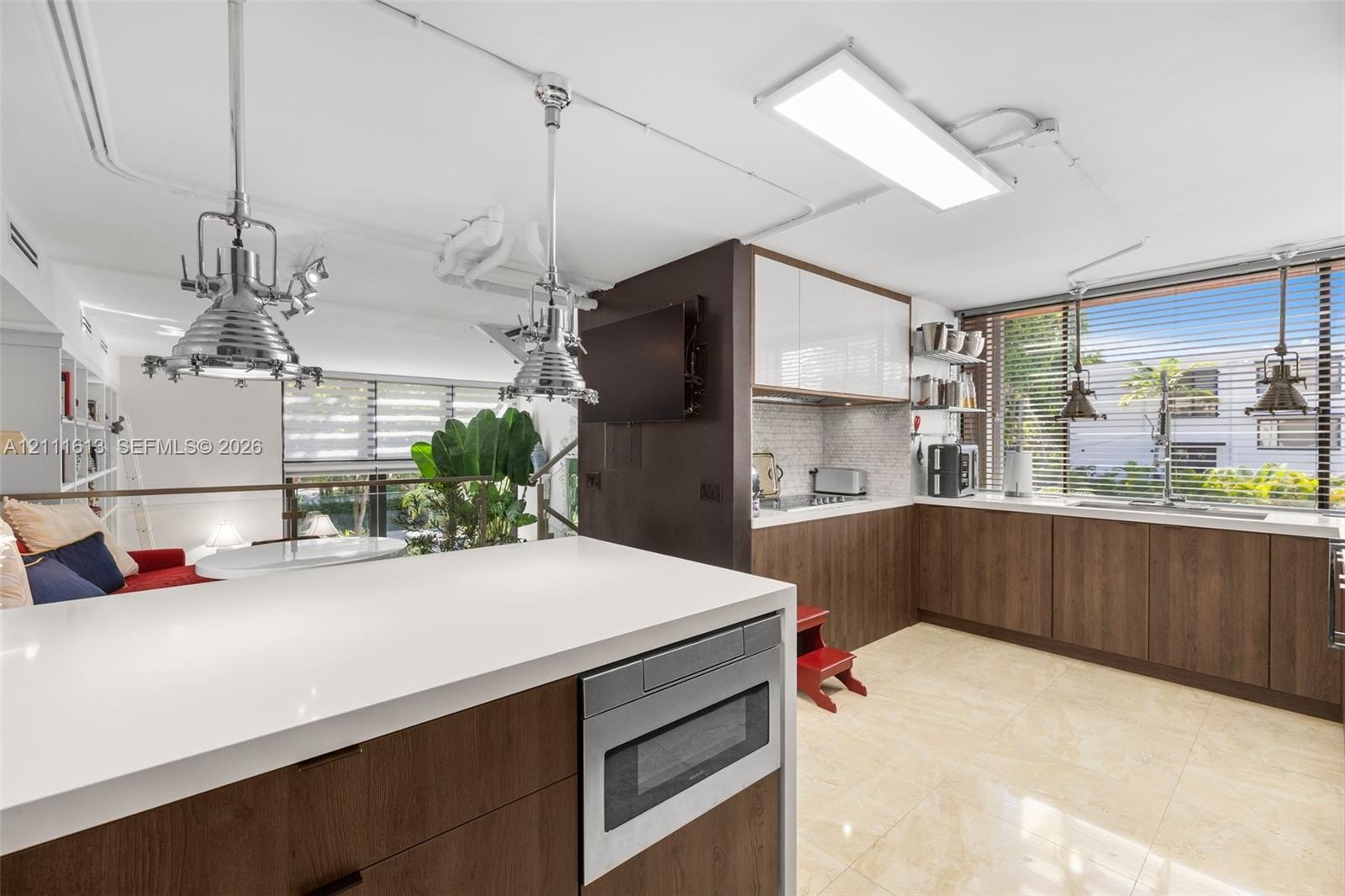 Kitchen featuring dual-toned cabinetry with high-gloss upper units and wood-finish lower units, light-toned stone-surface countertops, industrial-styl