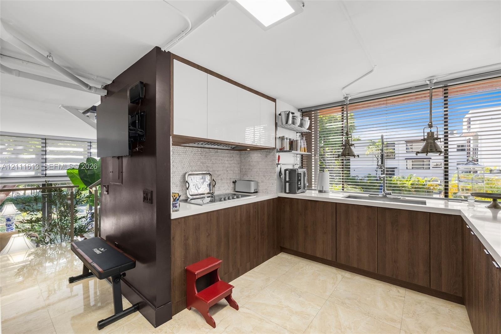 Kitchen featuring two-tone cabinetry with wood-finish lower units and high-gloss upper cabinets, solid-surface countertops, mosaic tile backsplash, an