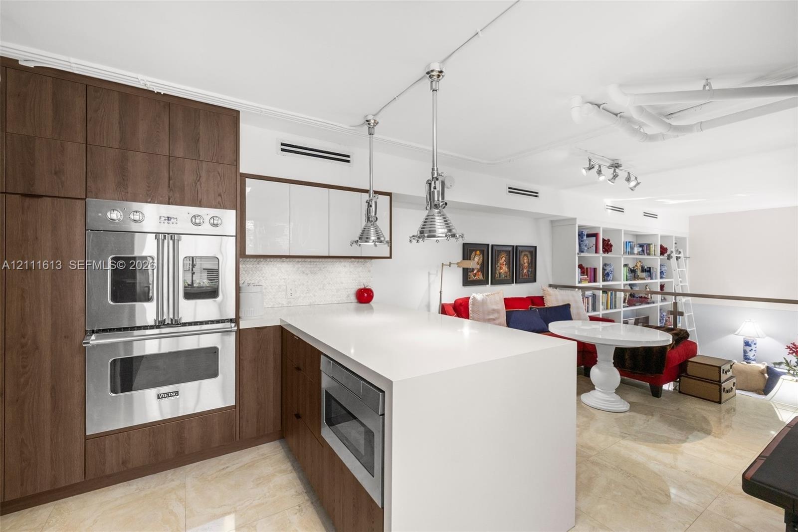 Kitchen featuring wood-finish cabinetry, a waterfall-edge island with stone countertop, stainless steel double wall oven, polished pendant lighting, a