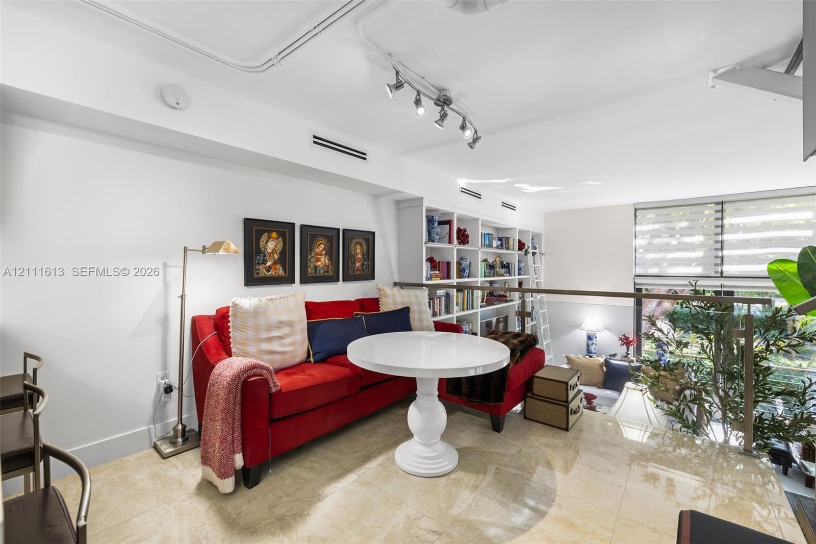 Open-concept interior featuring polished stone flooring, custom built-in floor-to-ceiling shelving with rolling library ladder, adjustable multi-head 