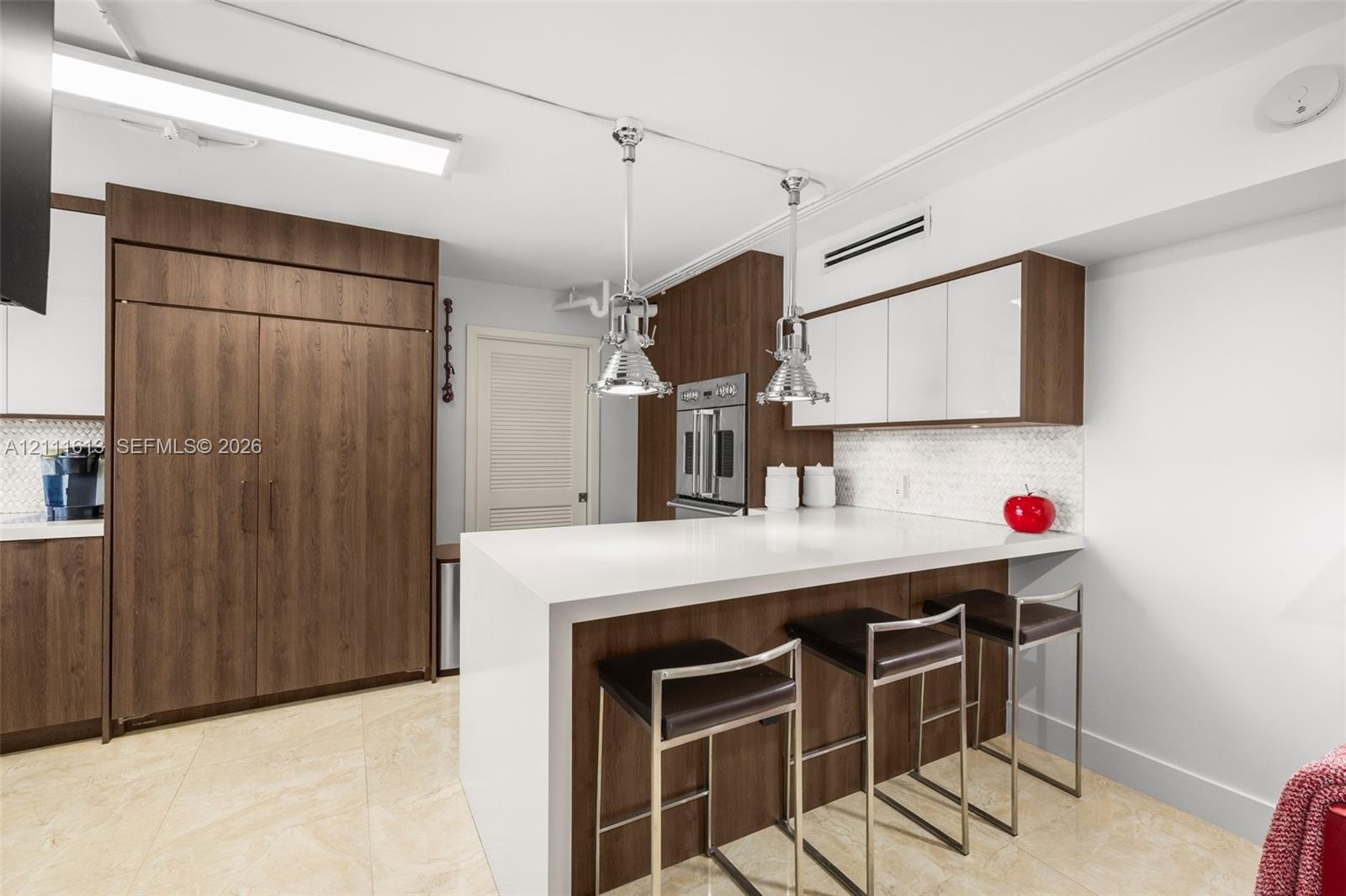 Kitchen featuring a waterfall-edge stone countertop, custom cabinetry with wood-finish and white high-gloss doors, stainless steel wall-mounted oven, 