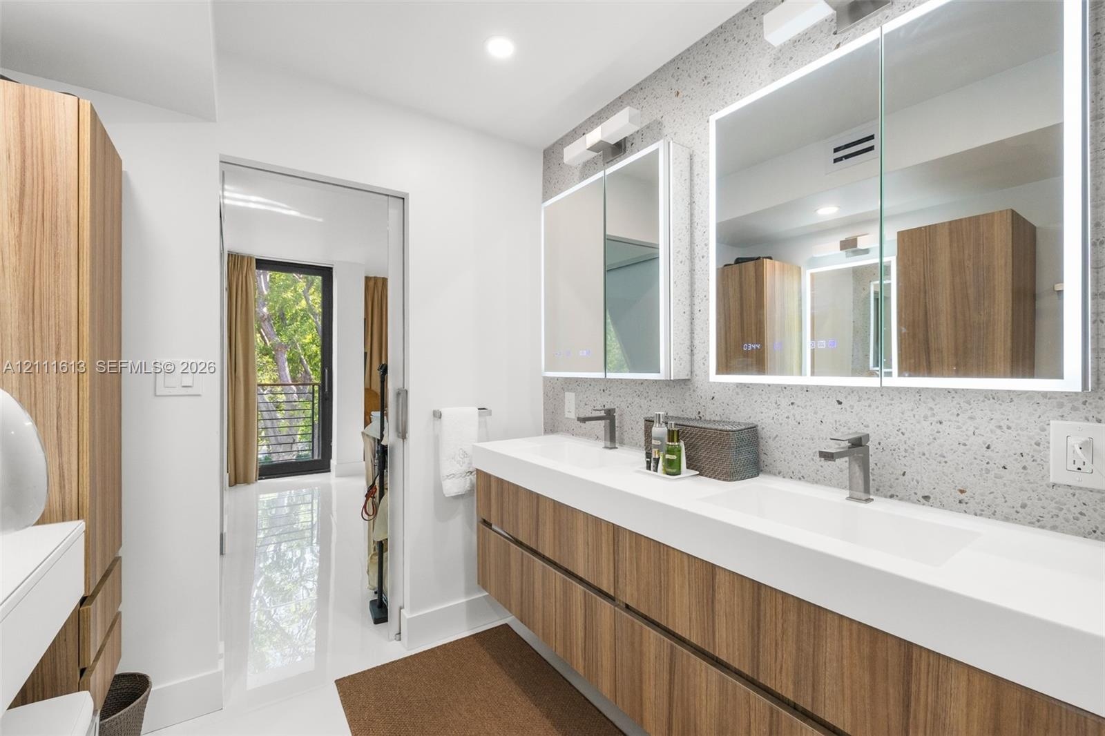 Floating double vanity with wood-finish cabinetry and integrated sinks, speckled stone-finish wall cladding, and dual recessed medicine cabinets with 