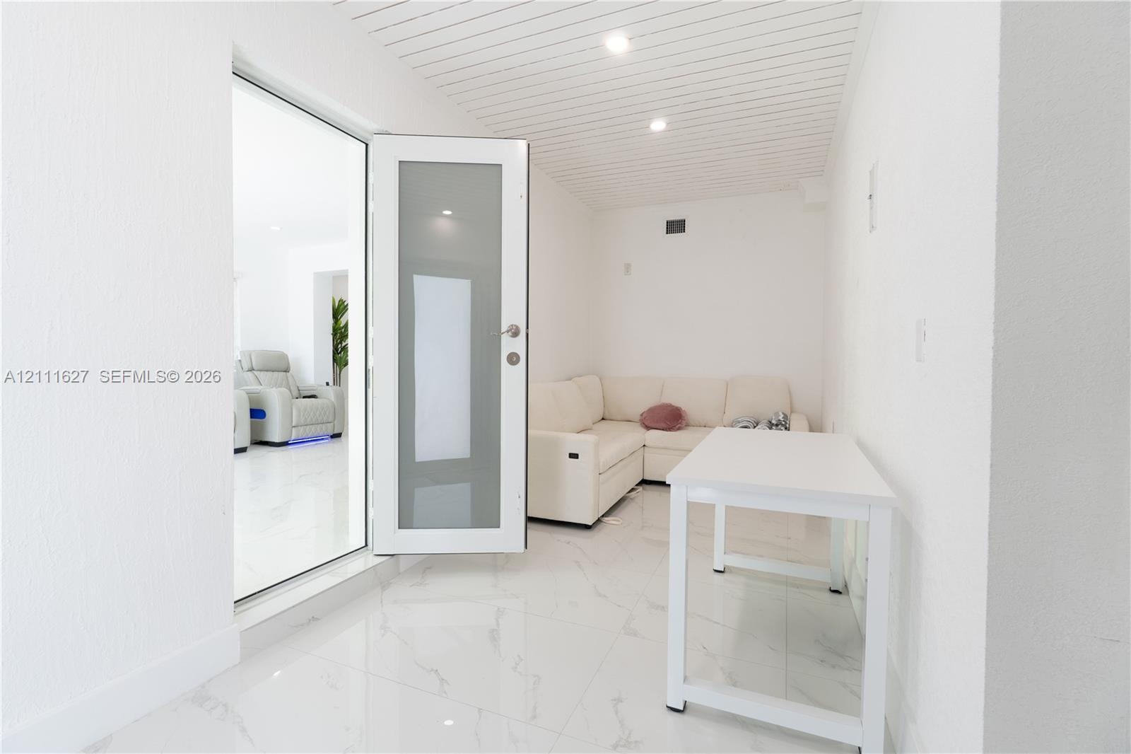 Interior space featuring polished white tile flooring, a frosted glass-panel door, and a white beadboard ceiling with recessed lighting