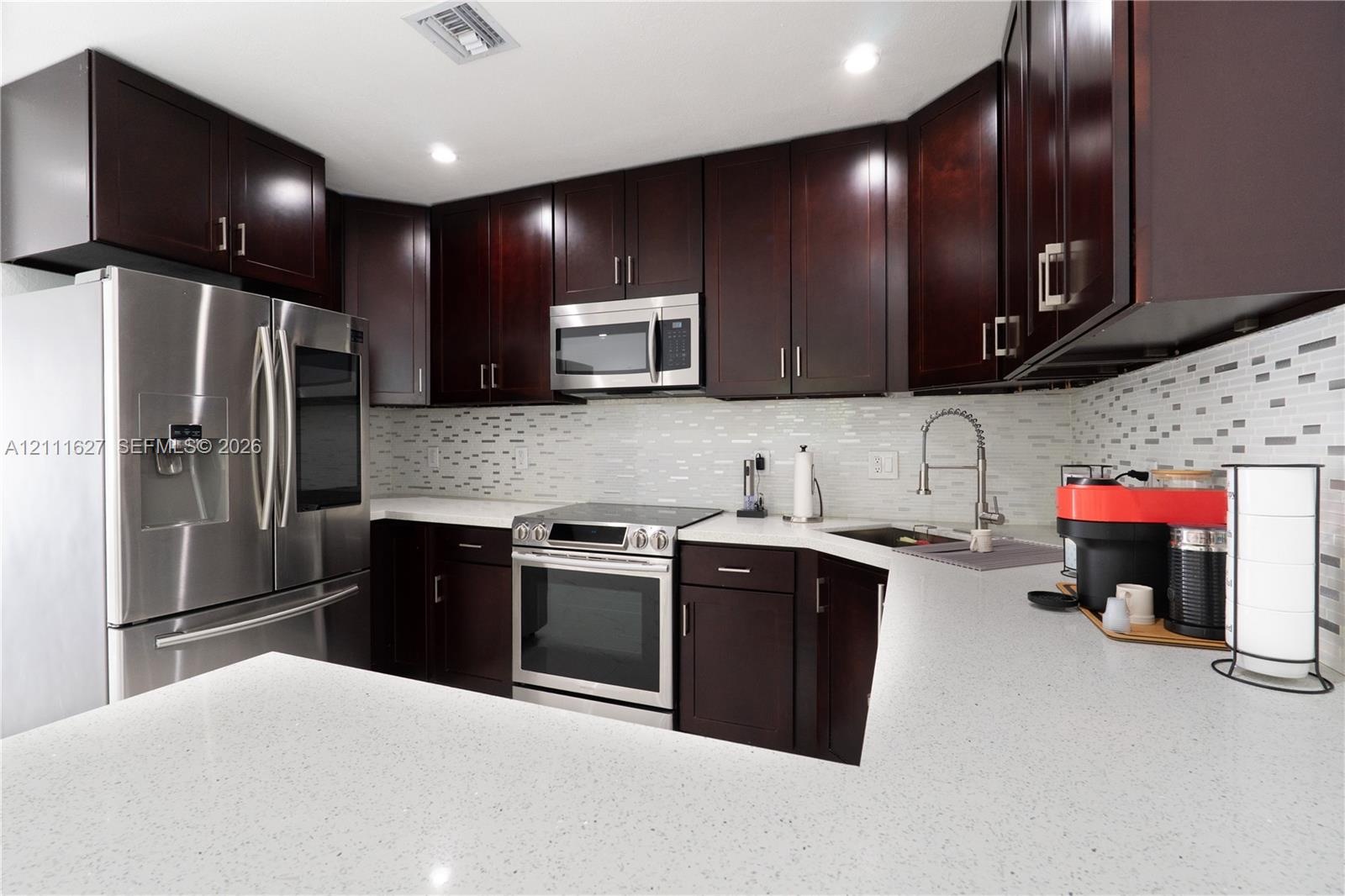 Kitchen featuring dark wood cabinetry, quartz countertops, a multi-tonal mosaic tile backsplash, and stainless steel appliances including a microwave,