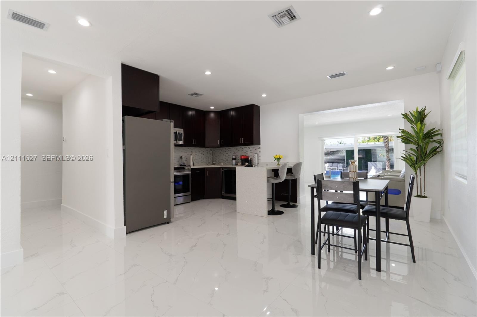 Kitchen featuring dark-toned cabinetry, a stone-finish countertop island with a breakfast bar, stainless steel appliances, a mosaic-tile backsplash, a