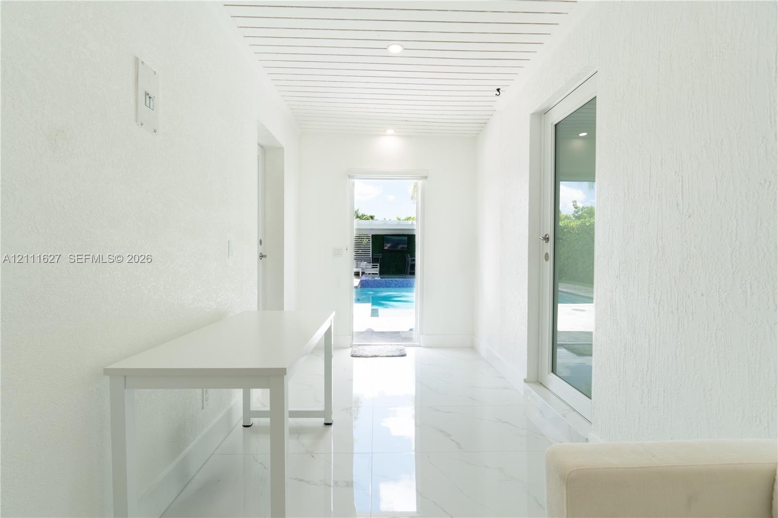 Hallway featuring white stone-finish flooring, slatted wood-paneled ceiling, and a full-height glass door
