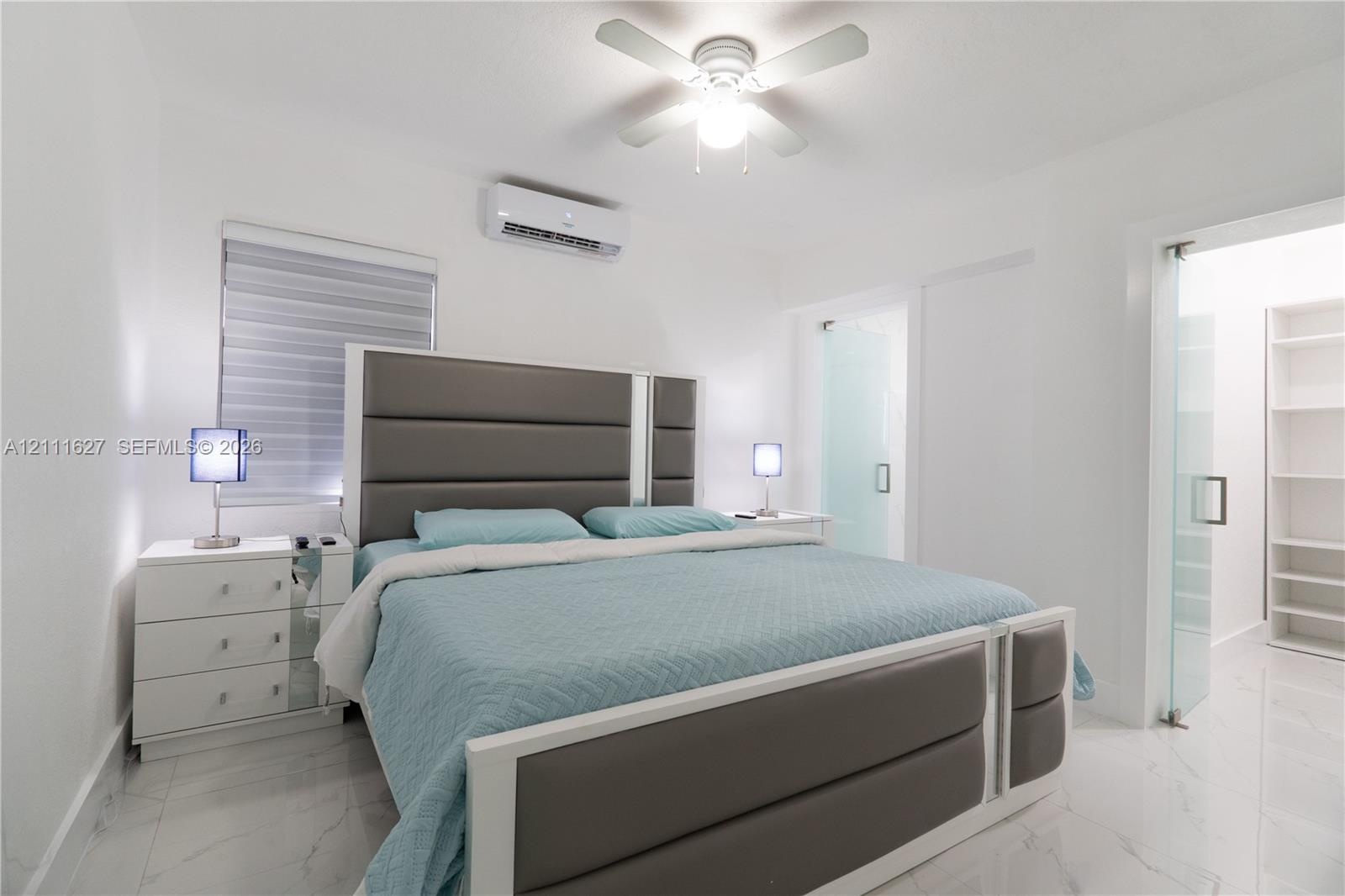 Neutral-toned interior featuring large-format tile flooring, a wall-mounted ductless air conditioning unit, a ceiling fan with integrated lighting, an