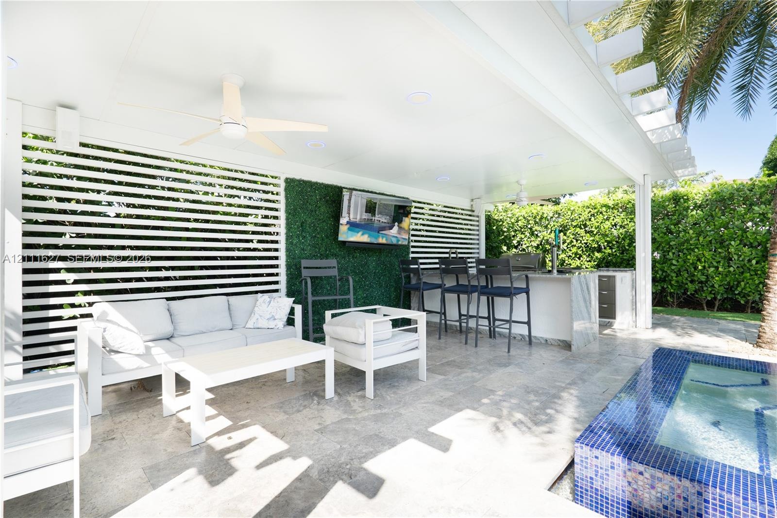Covered outdoor patio featuring stone flooring, a built-in outdoor kitchen with stone countertops, a slatted privacy screen, integrated ceiling lighti