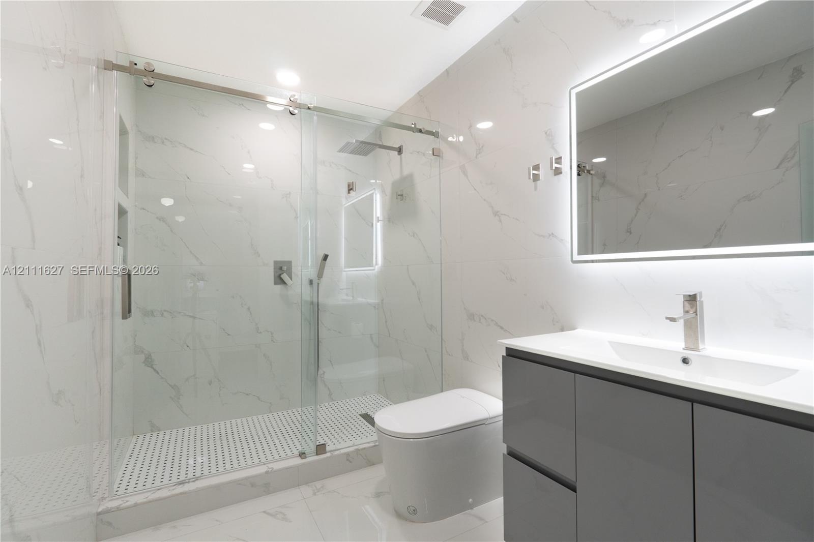 Walk-in glass-enclosed shower featuring stone-finish wall tile, rainfall showerhead, and built-in recessed shelving, complemented by a modern floating