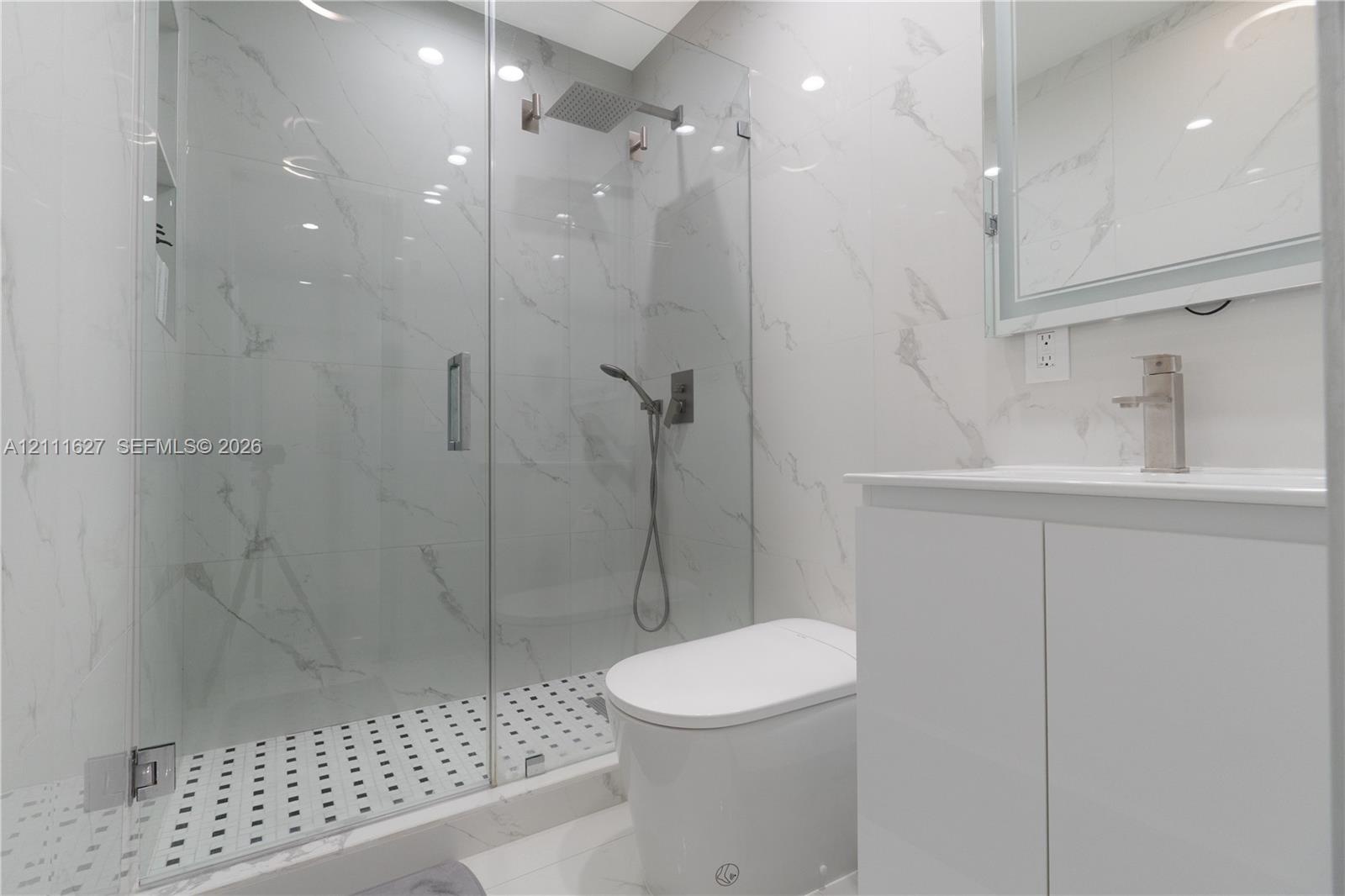 Walk-in glass-enclosed shower with a rainfall showerhead, large-format tile surround, mosaic tile flooring, and integrated wall niche, complemented by