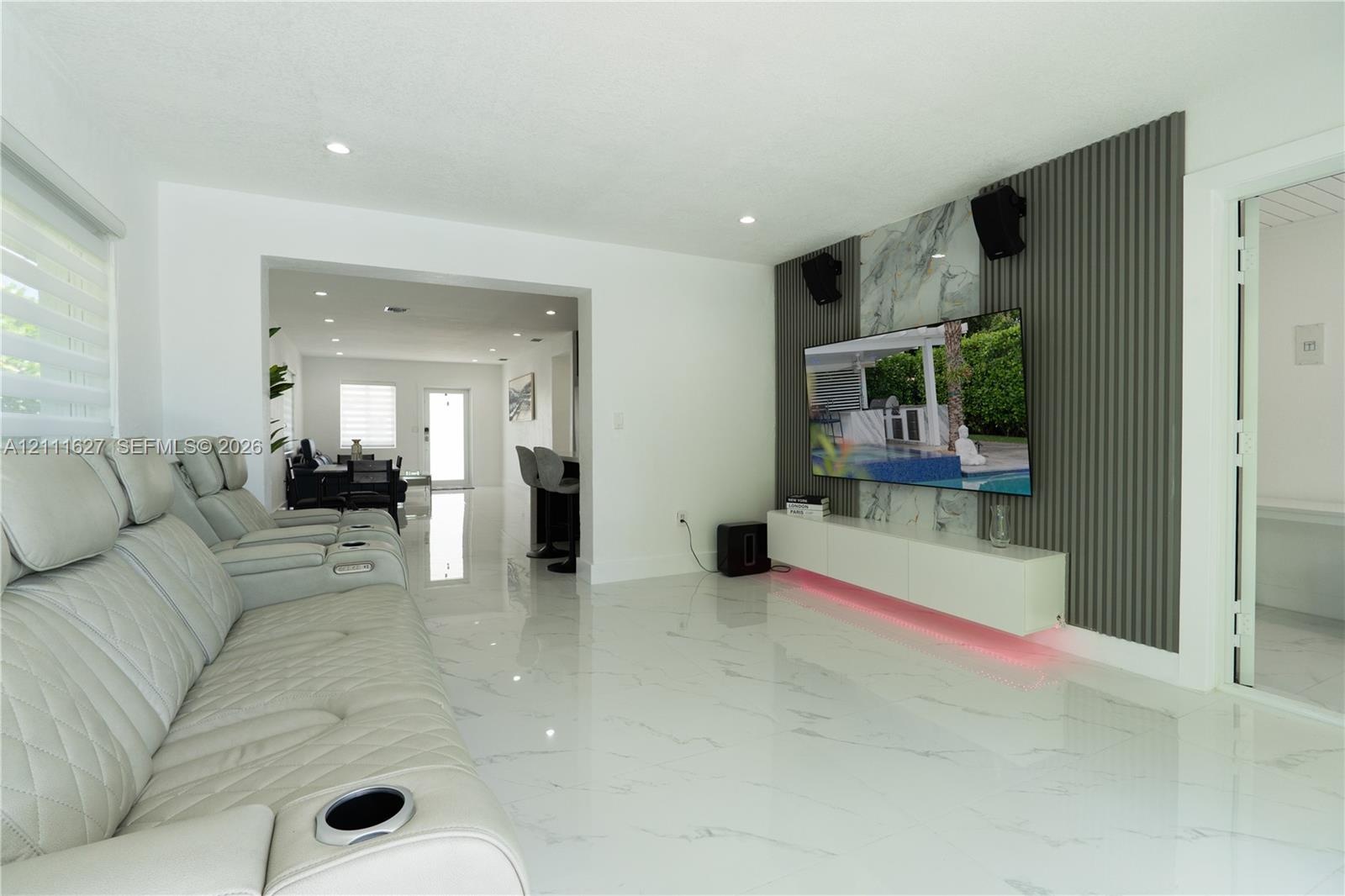 Living area featuring polished tile flooring, a wall-mounted floating media cabinet, and a decorative accent wall with vertical slat paneling and ston