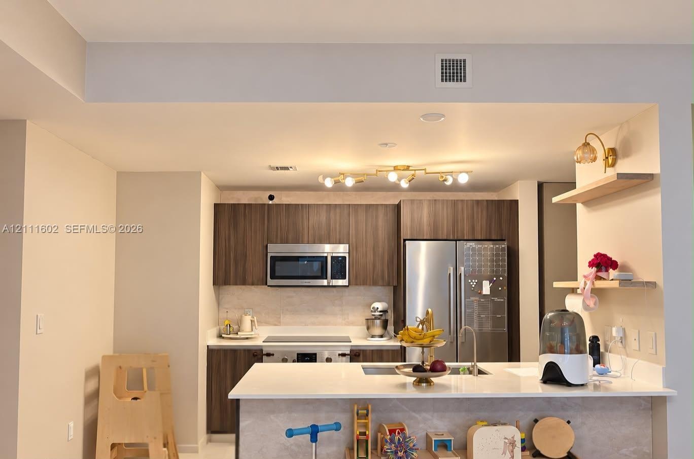 Kitchen featuring dark wood-finish cabinetry, stainless steel appliances, quartz countertops, a central island, and modern multi-bulb overhead lightin