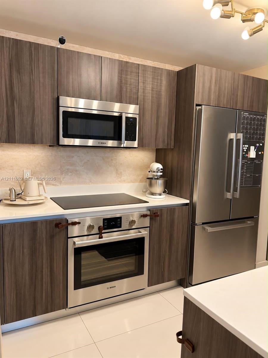 Kitchen featuring wood-finish cabinetry, stainless steel Bosch appliances, solid surface countertops, a stone-tile backsplash, and polished tile floor