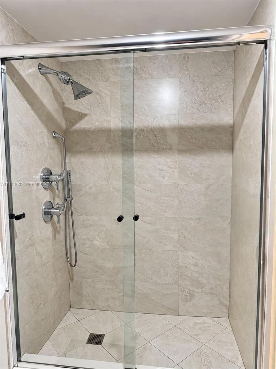 Walk-in shower featuring floor-to-ceiling stone-finish tile surround, sliding glass enclosure, polished chrome shower head, handheld sprayer, and diag