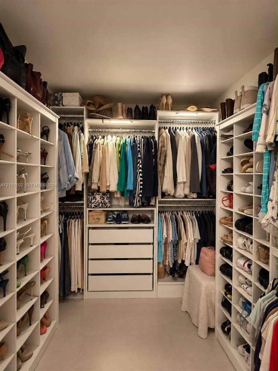 Walk-in closet featuring extensive built-in white shelving, multiple hanging rods, four deep storage drawers, and integrated overhead lighting