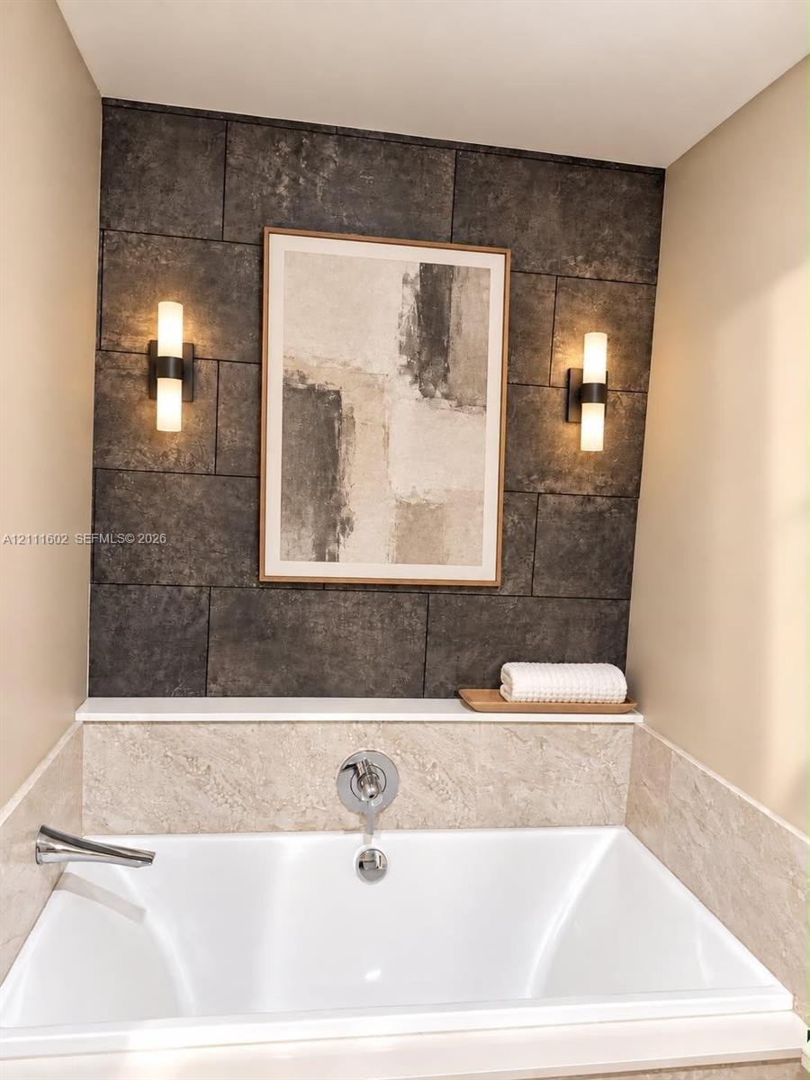 Built-in soaking tub featuring a neutral-toned stone tile surround, a dark stone tile accent wall, integrated display ledge, and dual wall-mounted cyl
