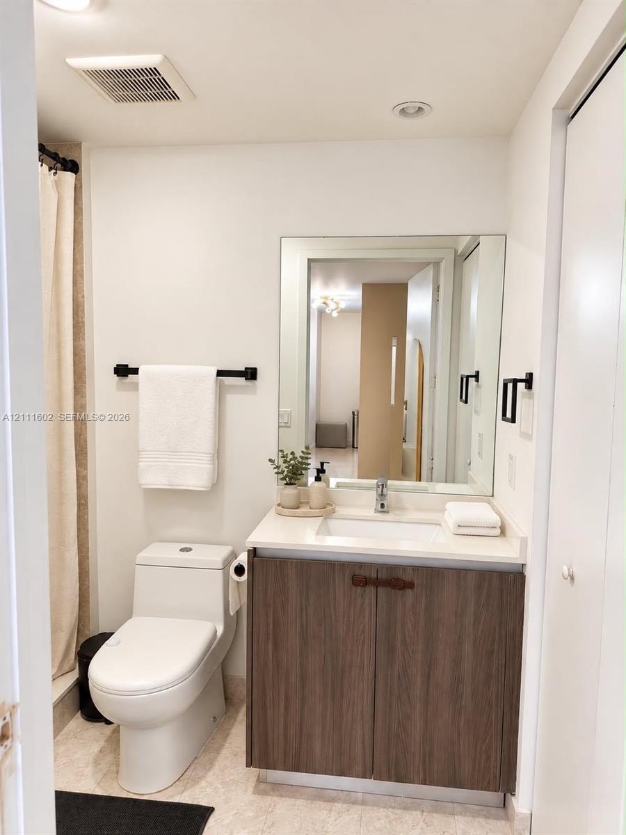Bathroom featuring a vanity with a wood-finish cabinet, solid surface countertop, integrated rectangular sink, wall-mounted mirror, and matte black ha