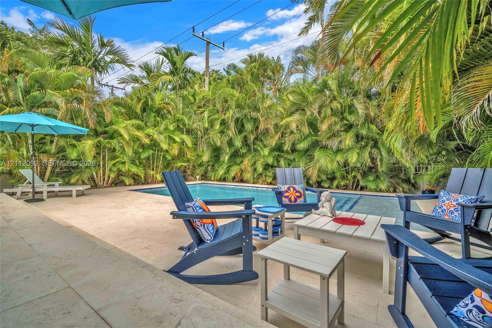 Rectangular swimming pool with stone-finish decking, surrounded by dense perimeter landscaping and mature palm trees