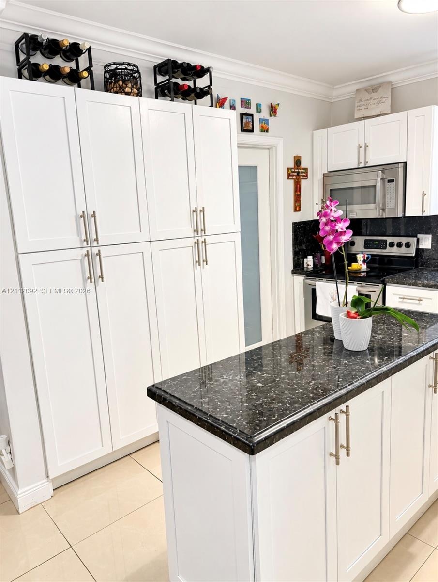 Kitchen featuring white shaker-style cabinetry, dark stone countertops, a central island, recessed lighting, and a built-in glass-front display cabine