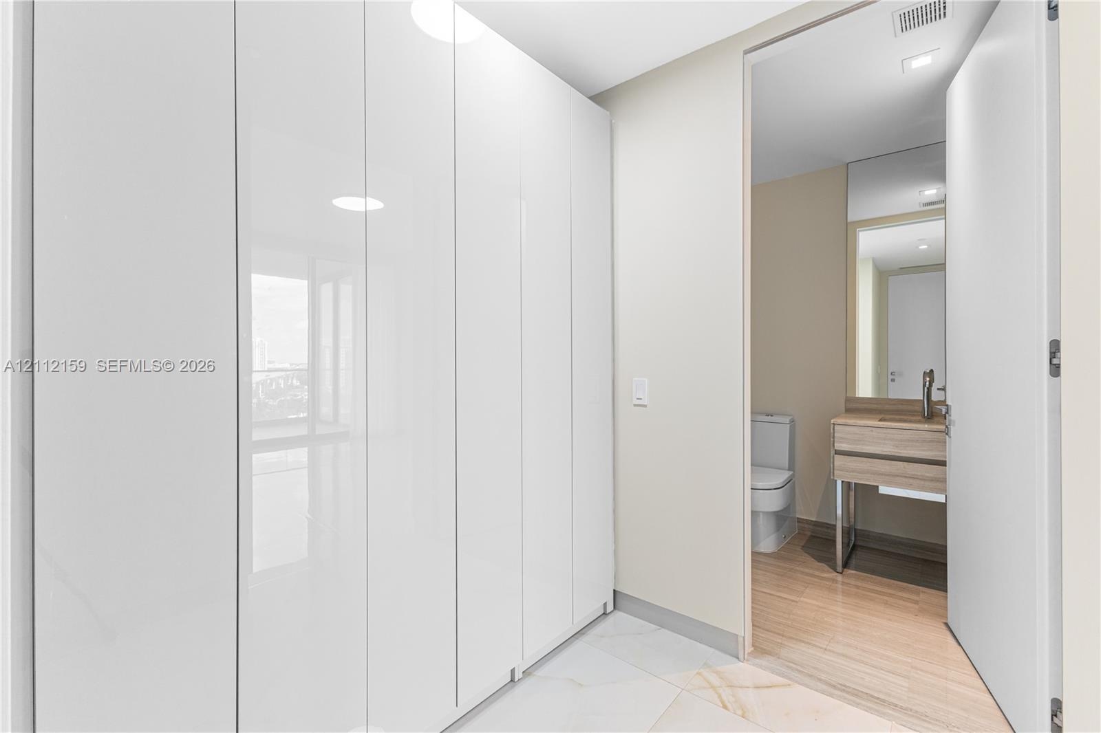 Floor-to-ceiling high-gloss white built-in cabinetry, large-format tile flooring, vanity with wood-finish cabinetry, rectangular vessel sink, and wall